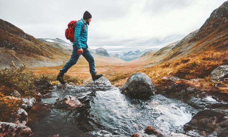 Hiker crossing rocky stream in mountain valley