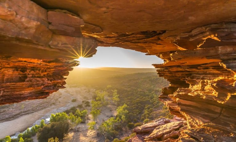 Sunset view through rocky cave over river valley