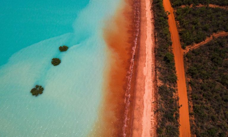 Aerial view turquoise ocean red beach dirt road
